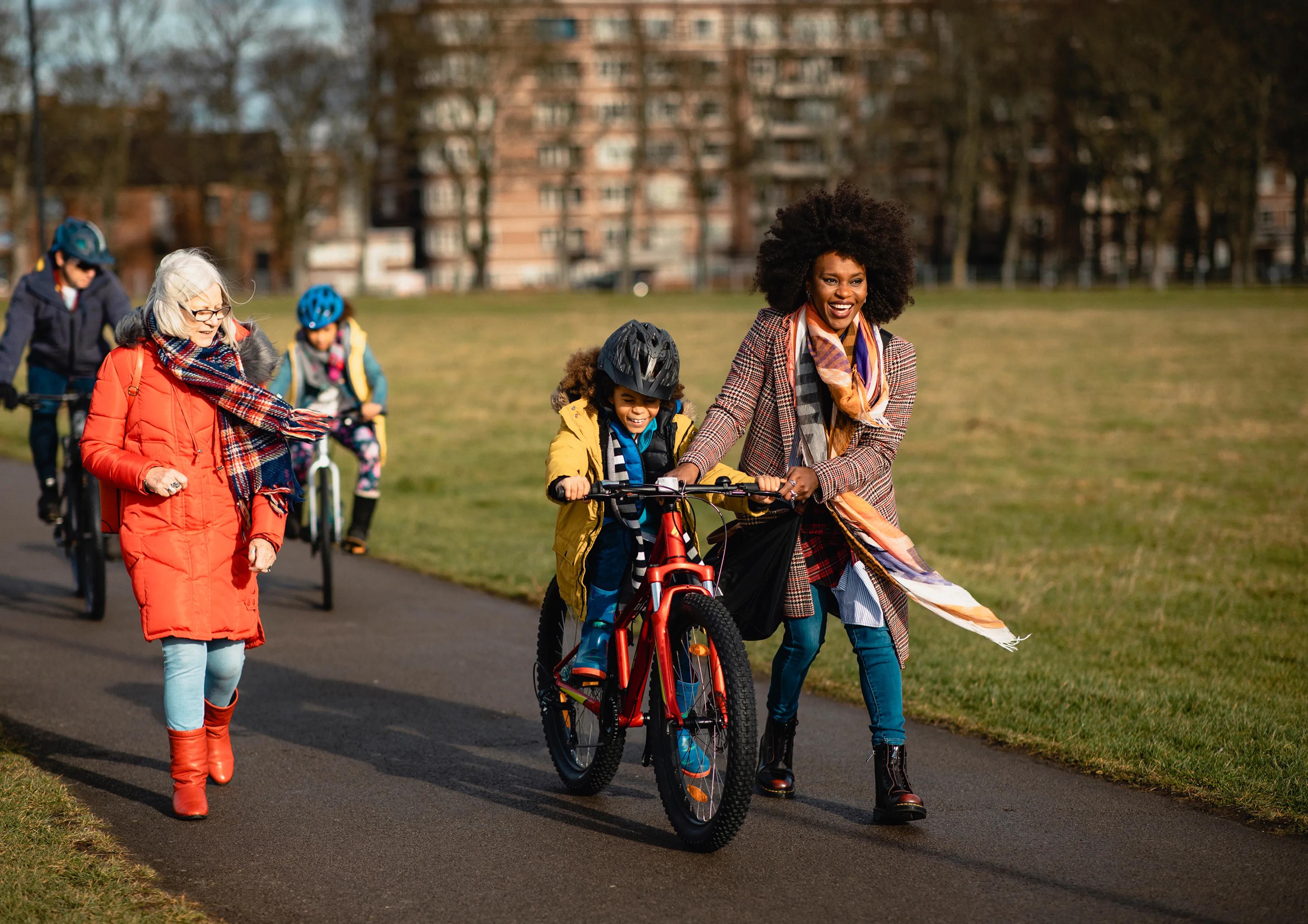 Girl cycling in a park with help from her mom